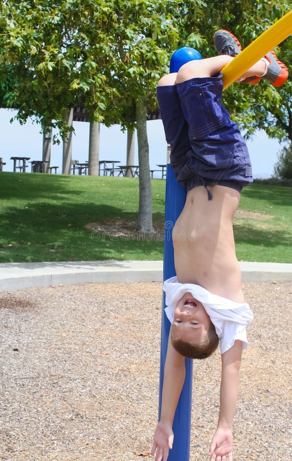 Preteen boy hanging upside down from high bar in park. Preteen boy hanging upside down from high bar in park