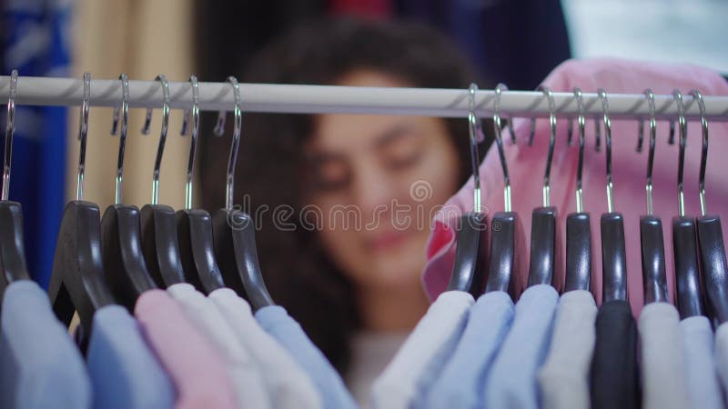 De hangers met t-shirts zijn op rek, kiest de vrouw kleren, unfocused gezicht