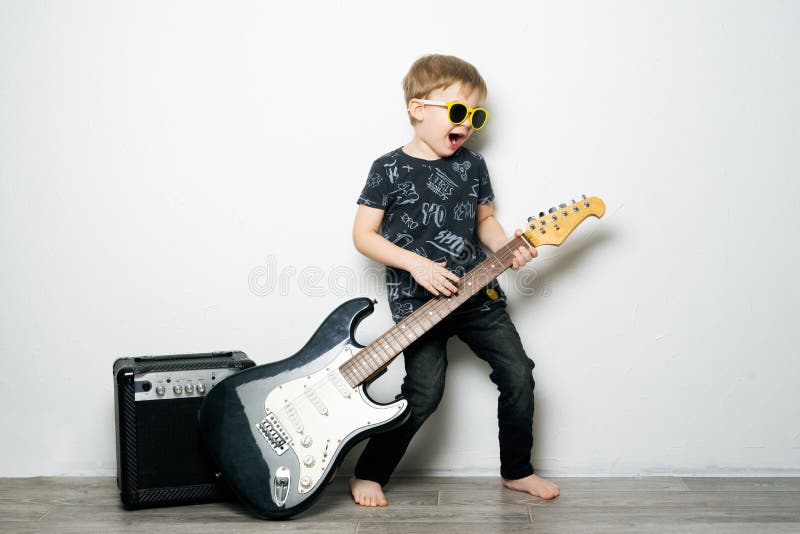 De hobbys van kinderen: een kleine jongen in zwarte glazen speelt de elektrische gitaar, imiteert een rotsster royalty-vrije stock afbeeldingen De hobbys van kinderen: een kleine jongen in zwarte glazen speelt de elektrische gitaar, imiteert een rotsster royalty-vrije stock afbeeldingen