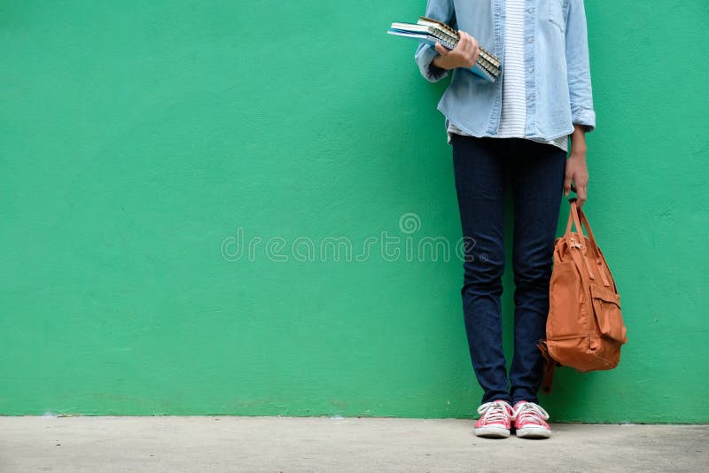 De holdingsboeken en schooltas die van het studentenmeisje zich over groene wa bevinden stock afbeeldingen De holdingsboeken en schooltas die van het studentenmeisje zich over groene wa bevinden stock afbeeldingen