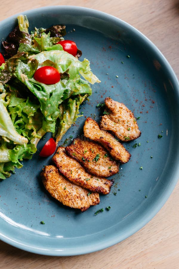 De hoogste die mening van BBQ roosterde kippenborst met salade in blauwe plaat op houten lijst wordt gediend royalty-vrije stock afbeelding De hoogste die mening van BBQ roosterde kippenborst met salade in blauwe plaat op houten lijst wordt gediend royalty-vrije stock afbeelding