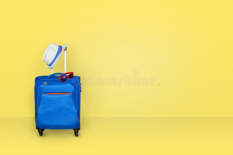 De ingepakte blauwe zak van de kofferreis voor reis, met zonglazen en hoed met lichtgele muur als achtergrond stock afbeelding De ingepakte blauwe zak van de kofferreis voor reis, met zonglazen en hoed met lichtgele muur als achtergrond stock afbeelding