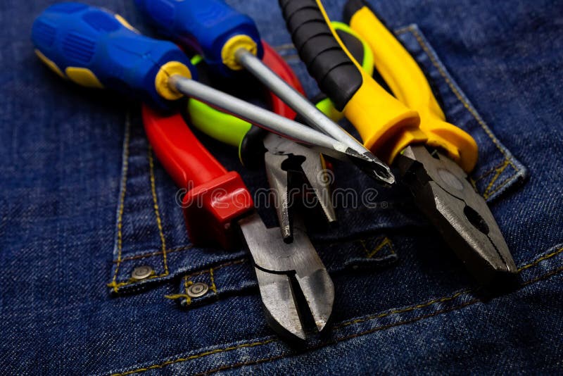 De instrumenten met heldere gekleurde handvatten liggen op het denim de buigtangpaar van de reparatieindustrie schroevedraaiers stock afbeelding De instrumenten met heldere gekleurde handvatten liggen op het denim de buigtangpaar van de reparatieindustrie schroevedraaiers stock afbeelding
