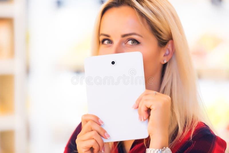 De jonge aantrekkelijke vrouw verbergt haar glimlach met een tabletcomputer stock foto De jonge aantrekkelijke vrouw verbergt haar glimlach met een tabletcomputer stock foto