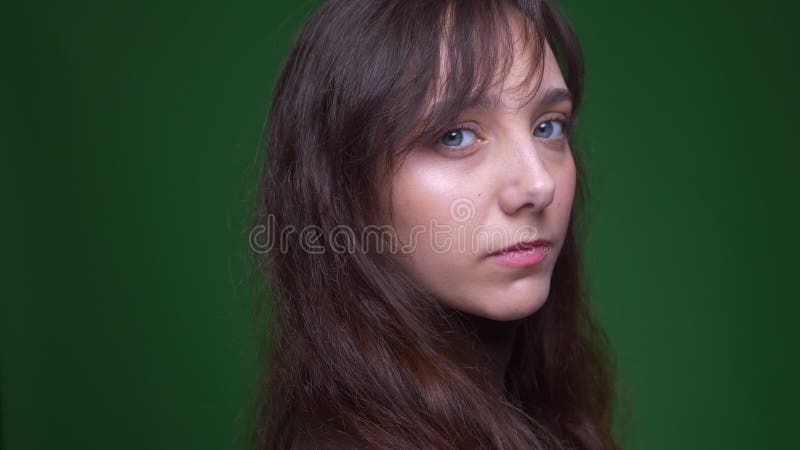De jonge donkerbruine vrouwelijke student draait aan camera en horloges vreedzaam in het op groene achtergrond