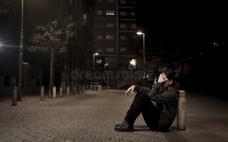 Young sad woman sitting on street ground at night alone desperate suffering depression left abandoned and lost in grunge urban background as abuse and violence female victim or addict concept. Young sad woman sitting on street ground at night alone desperate suffering depression left abandoned and lost in grunge urban background as abuse and violence female victim or addict concept