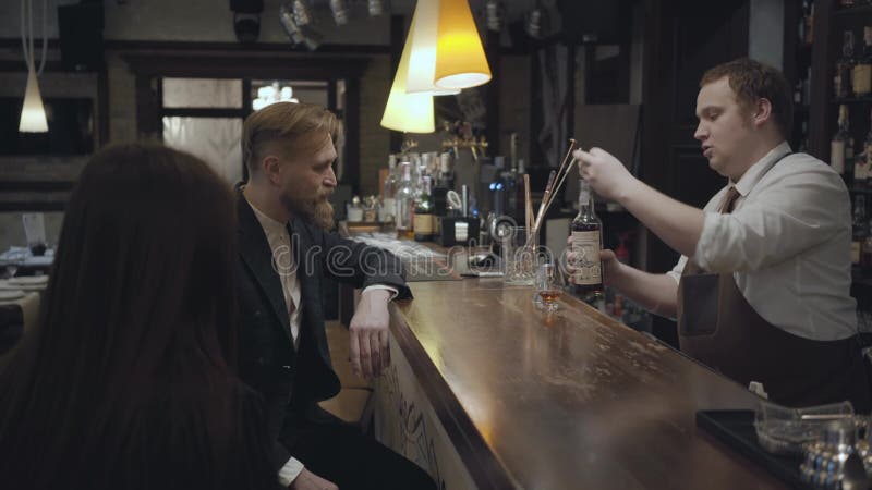 De jonge gebaarde man en de onherkenbare donkerbruine vrouwenzitting bij de barteller Mollige barman gietende alcohol binnen