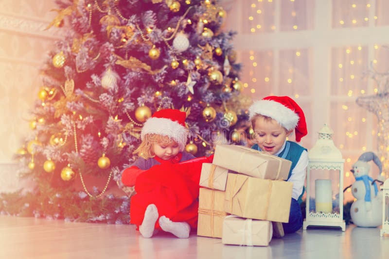 De jonge geitjes die Kerstmis openen stelt in verfraaide woonkamer voor stock foto De jonge geitjes die Kerstmis openen stelt in verfraaide woonkamer voor stock foto