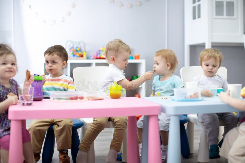 De jonge geitjesgroep heeft lunch in kleuterschool Leuke kindjongen die een maaltijdmeisje delen stock foto's De jonge geitjesgroep heeft lunch in kleuterschool Leuke kindjongen die een maaltijdmeisje delen stock foto's