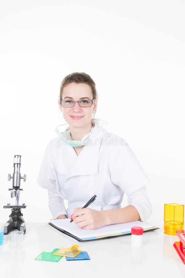 De jonge glimlachende wetenschapper van de vrouwenonderzoeker in witte laboratoriumlaag die zich door microscoop bevinden royalty-vrije stock fotografie De jonge glimlachende wetenschapper van de vrouwenonderzoeker in witte laboratoriumlaag die zich door microscoop bevinden royalty-vrije stock fotografie
