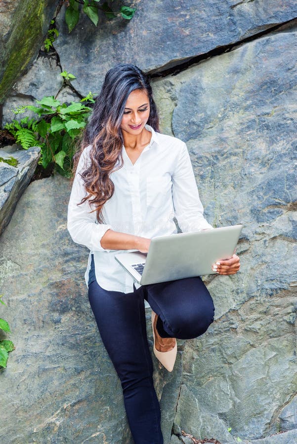 De jonge Indische Amerikaanse Vrouw van het Oosten met lang haar die aan laptop computer openlucht in New York werken royalty-vrije stock afbeeldingen De jonge Indische Amerikaanse Vrouw van het Oosten met lang haar die aan laptop computer openlucht in New York werken royalty-vrije stock afbeeldingen