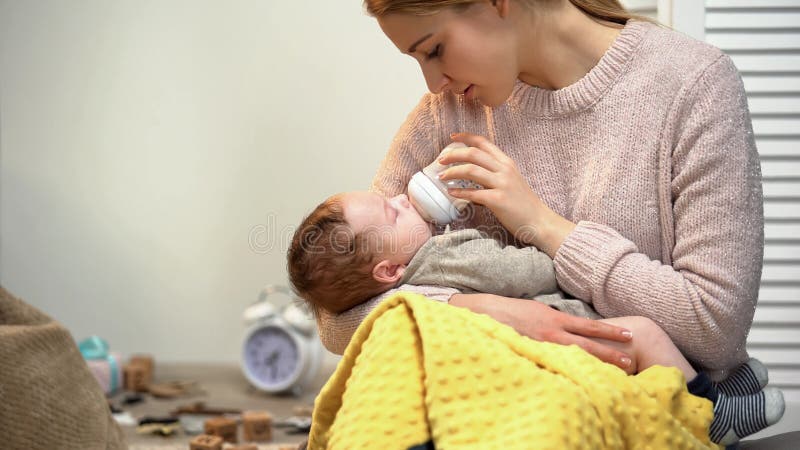 De jonge jongen van de dame voedende baby, fles met zuigelingsformule, die jong geitje zetten aan slaap stock foto's De jonge jongen van de dame voedende baby, fles met zuigelingsformule, die jong geitje zetten aan slaap stock foto's