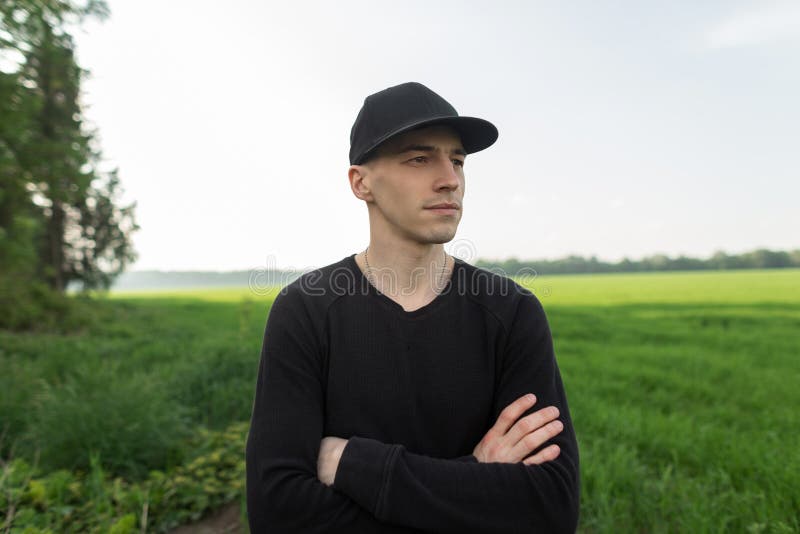 De jonge knappe mens in modieus zwart GLB in zwart uitstekend overhemd bevindt zich in openlucht op een gebied met groen gras Het stock afbeeldingen De jonge knappe mens in modieus zwart GLB in zwart uitstekend overhemd bevindt zich in openlucht op een gebied met groen gras Het stock afbeeldingen