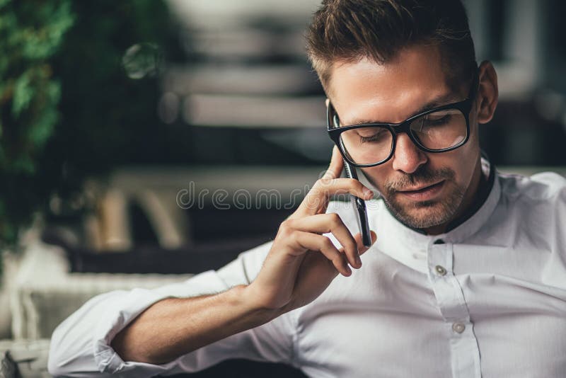 De jonge knappe zakenman spreekt op telefoon, zittend bij lijst in koffie De mens in glazen maakt vraag Bedrijfspersoon binnen stock foto De jonge knappe zakenman spreekt op telefoon, zittend bij lijst in koffie De mens in glazen maakt vraag Bedrijfspersoon binnen stock foto