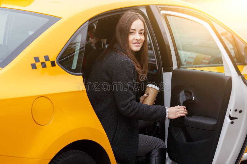 De jonge leuke donkerbruine koffie van de vrouwenholding in achterbank van taxi royalty-vrije stock afbeelding De jonge leuke donkerbruine koffie van de vrouwenholding in achterbank van taxi royalty-vrije stock afbeelding