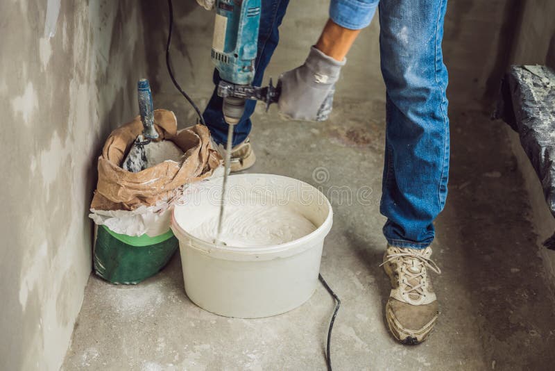 De jonge mannelijke schilder kneedt stopverf met water in een emmer gebruikend een handbediende mixer voor de bouw van mengelinge stock fotografie De jonge mannelijke schilder kneedt stopverf met water in een emmer gebruikend een handbediende mixer voor de bouw van mengelinge stock fotografie
