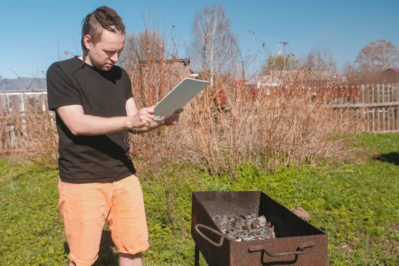 De jonge mens blaast de steenkolen in de grillkoperslager met op een scherpe Raad stock foto De jonge mens blaast de steenkolen in de grillkoperslager met op een scherpe Raad stock foto