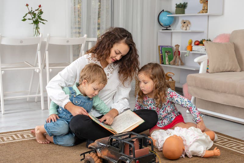 De jonge moeder of het kindermeisje met kleine kinderen, een jongen en een meisje, zit royalty-vrije stock fotografie De jonge moeder of het kindermeisje met kleine kinderen, een jongen en een meisje, zit royalty-vrije stock fotografie