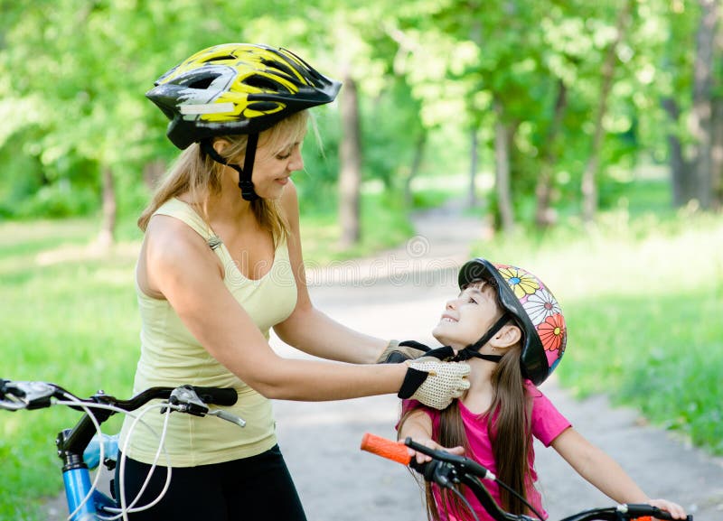 De jonge moeder kleedt de fietshelm van haar dochter