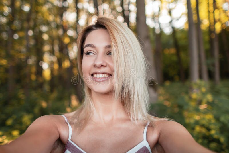 De jonge mooie gelukkige vrouw in een modieuze roze kleding maakt selfie op een smartphone in het bos onder de bomen stock foto De jonge mooie gelukkige vrouw in een modieuze roze kleding maakt selfie op een smartphone in het bos onder de bomen stock foto