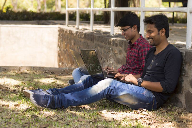De jonge studenten die aan laptop werken leunen op muur naast elkaar in park stock foto De jonge studenten die aan laptop werken leunen op muur naast elkaar in park stock foto