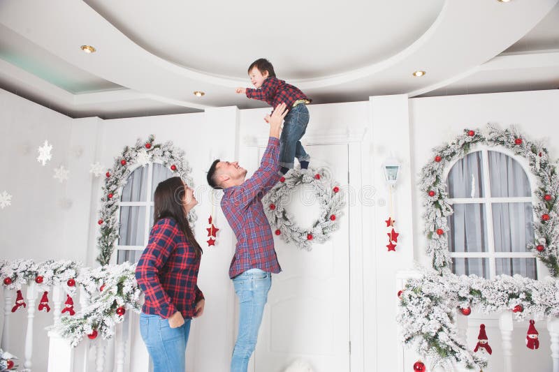 De jonge vader werpt omhoog weinig zoon met moeder in Kerstmisdecor royalty-vrije stock afbeelding De jonge vader werpt omhoog weinig zoon met moeder in Kerstmisdecor royalty-vrije stock afbeelding