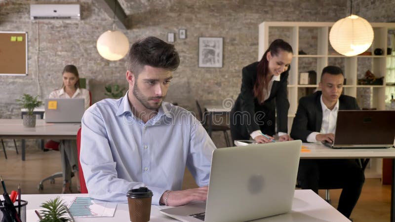 De jonge vermoeide zakenman werkt in bureau, die aan laptop, bespreking over achtergrond, het werk concept, zaken onttrekken