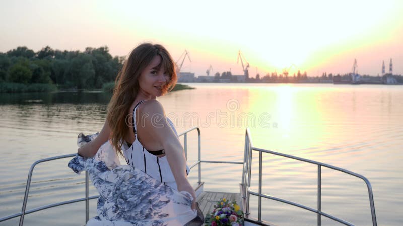 De jonge vrouw bevindt zich op boog van zeilboot op achtergrondzonsondergang in de zomerreis