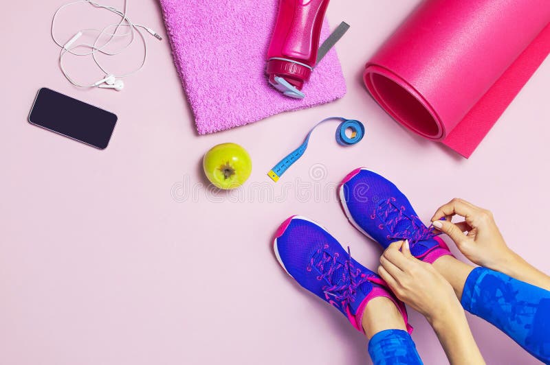 De jonge vrouw in blauwe tennisschoenen houdt appel in zijn handen, voorbereidingen treffend voor opleiding Fles water, yogamat, stock afbeelding De jonge vrouw in blauwe tennisschoenen houdt appel in zijn handen, voorbereidingen treffend voor opleiding Fles water, yogamat, stock afbeelding