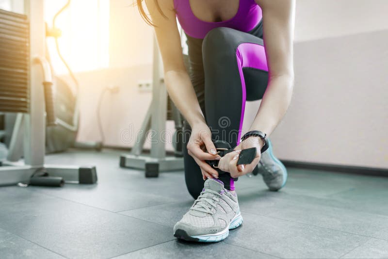 De jonge vrouw die de riemen van de leerenkel dragen treft om op geschiktheidsmachine in de gymnastiek uit te oefenen voorbereidi stock foto De jonge vrouw die de riemen van de leerenkel dragen treft om op geschiktheidsmachine in de gymnastiek uit te oefenen voorbereidi stock foto