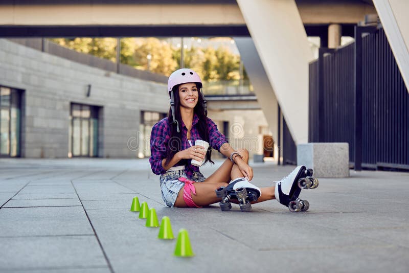 De jonge vrouw neemt een rust na het berijden van rolschaatsen en het drinken van koffie stock foto's De jonge vrouw neemt een rust na het berijden van rolschaatsen en het drinken van koffie stock foto's