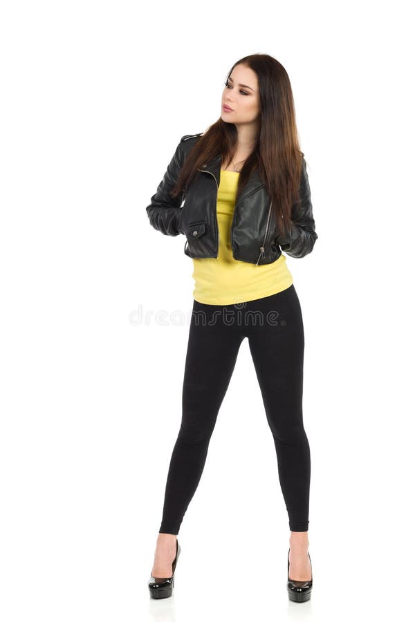 Young woman in black leather jacket, leggings and high heels is holding hands in pockets and looking away. Full length studio shot isolated on white. Young woman in black leather jacket, leggings and high heels is holding hands in pockets and looking away. Full length studio shot isolated on white.