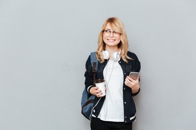 De jonge vrouwelijke kop van de studentenholding van koffie en smartphone stock afbeelding De jonge vrouwelijke kop van de studentenholding van koffie en smartphone stock afbeelding