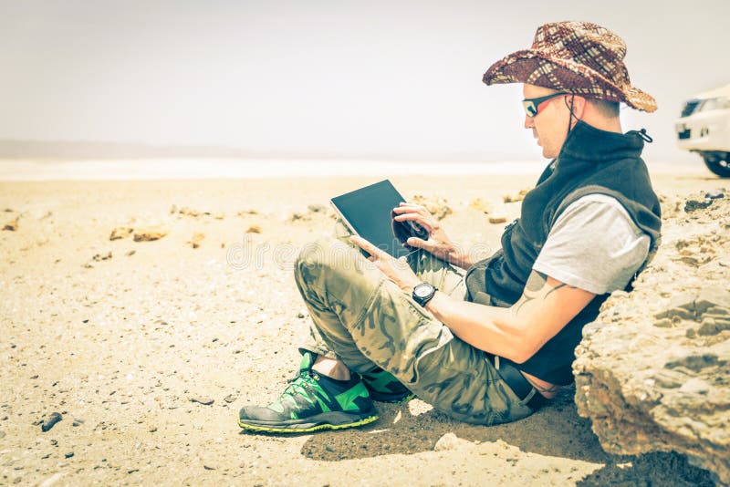 De jonge zitting van de hipstermens in woestijnweg - Technologieconcept stock fotografie De jonge zitting van de hipstermens in woestijnweg - Technologieconcept stock fotografie