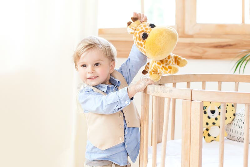 De jongen bevindt zich naast de wieg in het kinderdagverblijf en houdt een stuk speelgoed in zijn handen het jonge geitje is in k stock fotografie De jongen bevindt zich naast de wieg in het kinderdagverblijf en houdt een stuk speelgoed in zijn handen het jonge geitje is in k stock fotografie