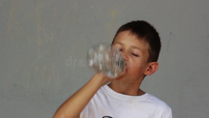 De jongen drinkt water van een fles op een grijze achtergrond
