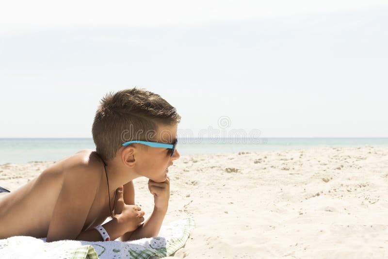 De jongen lacht en werpt zand op zijn hoofd liggend op het zand tegen de blauwe hemel stock afbeeldingen De jongen lacht en werpt zand op zijn hoofd liggend op het zand tegen de blauwe hemel stock afbeeldingen
