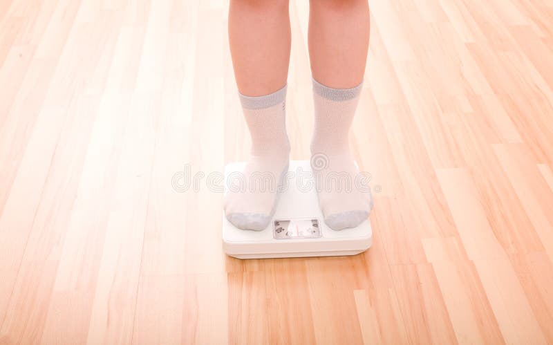 De jongen meet gewicht op vloerschalen stock foto De jongen meet gewicht op vloerschalen stock foto