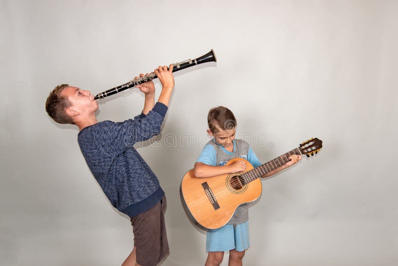 De jongen speelt de gitaar en de klarinet in verschillend stelt, stellend in de studio royalty-vrije stock afbeelding De jongen speelt de gitaar en de klarinet in verschillend stelt, stellend in de studio royalty-vrije stock afbeelding