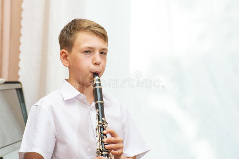 De jongen speelt de klarinet dichtbij de zwarte piano door het venster Musicologie, muziekonderwijs en onderwijs stock afbeelding De jongen speelt de klarinet dichtbij de zwarte piano door het venster Musicologie, muziekonderwijs en onderwijs stock afbeelding