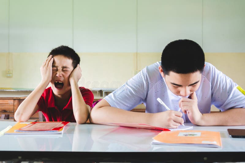 De jongen voelt in slaap in het klaslokaal maar een andere ??n doend thuiswerk stock foto's De jongen voelt in slaap in het klaslokaal maar een andere ??n doend thuiswerk stock foto's