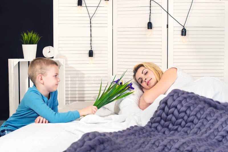 De jongen wekt mamma en geeft haar een boeket van bloemen in bed Het vieren de Dag van de Vrouw De dag van de moeder `s royalty-vrije stock fotografie De jongen wekt mamma en geeft haar een boeket van bloemen in bed Het vieren de Dag van de Vrouw De dag van de moeder `s royalty-vrije stock fotografie