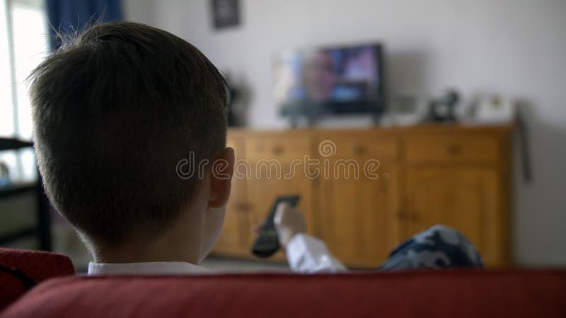 Boy sits on the sofa in front of the TV and switches the channels, have fun. Boy sits on the sofa in front of the TV and switches the channels, have fun