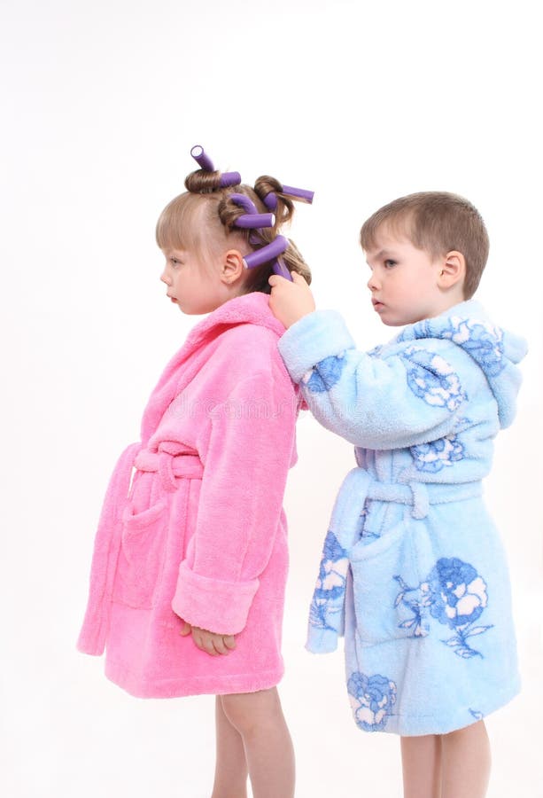 Two children cost on a white background, the boy twists to the girl hair curlers in a blue dressing gown. Two children cost on a white background, the boy twists to the girl hair curlers in a blue dressing gown