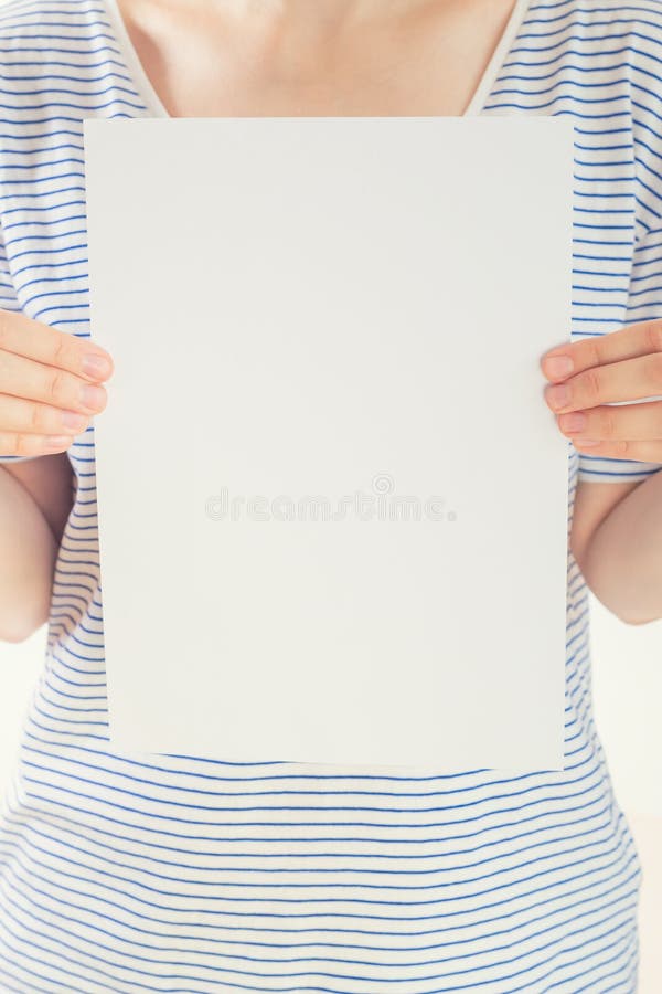 De Kaukasische vrouw in gestreepte t-shirt houdt een wit leeg document blad in handen royalty-vrije stock foto's De Kaukasische vrouw in gestreepte t-shirt houdt een wit leeg document blad in handen royalty-vrije stock foto's