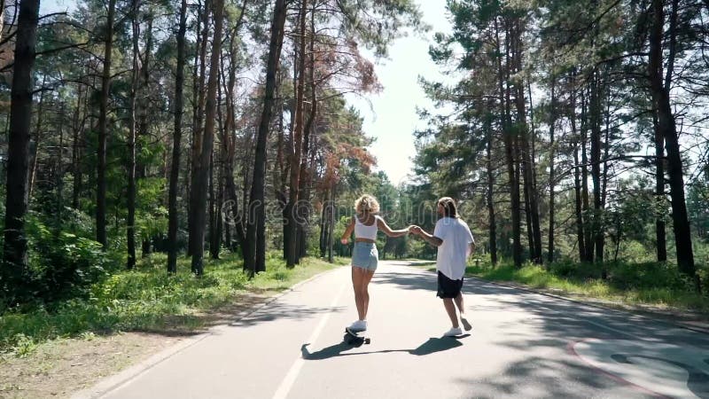 De kerel houdt de hand van het meisje wanneer zij een skateboard berijdt