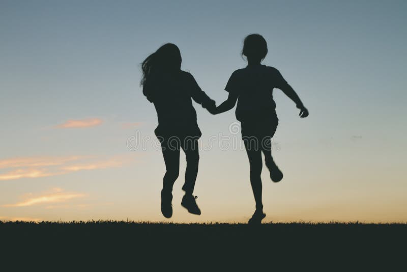 De kinderen die bij zonsondergang springen silhouetteren royalty-vrije stock afbeeldingen De kinderen die bij zonsondergang springen silhouetteren royalty-vrije stock afbeeldingen