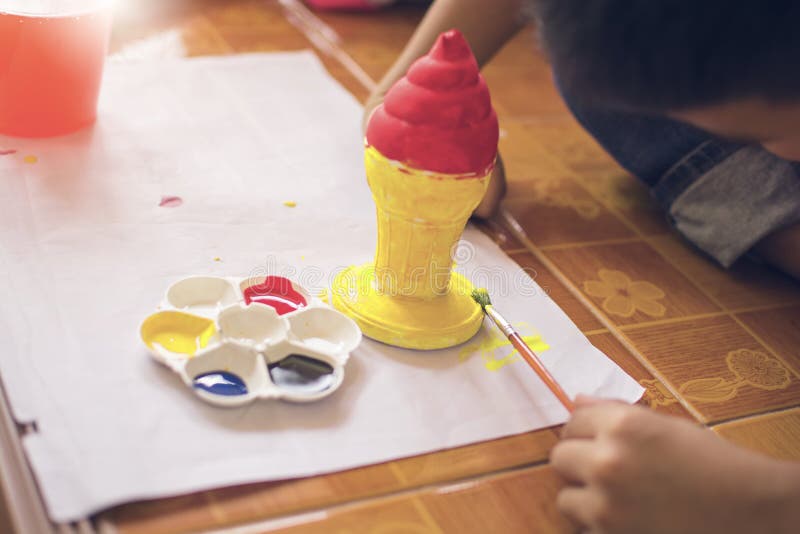 De kinderen gebruiken borstel aan het schilderen van plastic roomijskegel met het schilderen van plaat en fles water royalty-vrije stock afbeeldingen De kinderen gebruiken borstel aan het schilderen van plastic roomijskegel met het schilderen van plaat en fles water royalty-vrije stock afbeeldingen