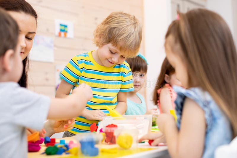 De kinderen met leraar spelen kleurrijk kleistuk speelgoed in opvang stock fotografie De kinderen met leraar spelen kleurrijk kleistuk speelgoed in opvang stock fotografie