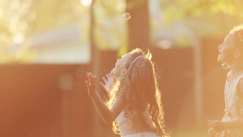 De kleine Europese kinderen springen en spelen met de zeepbels in een zonsonderganglicht Lensgloed, buiten het schieten